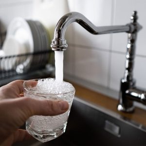 A person fills a glass with water from the kitchen faucet