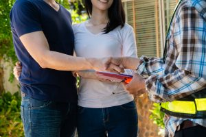 Happy homeowners stand and shake hands with a contractor holding a clipboard