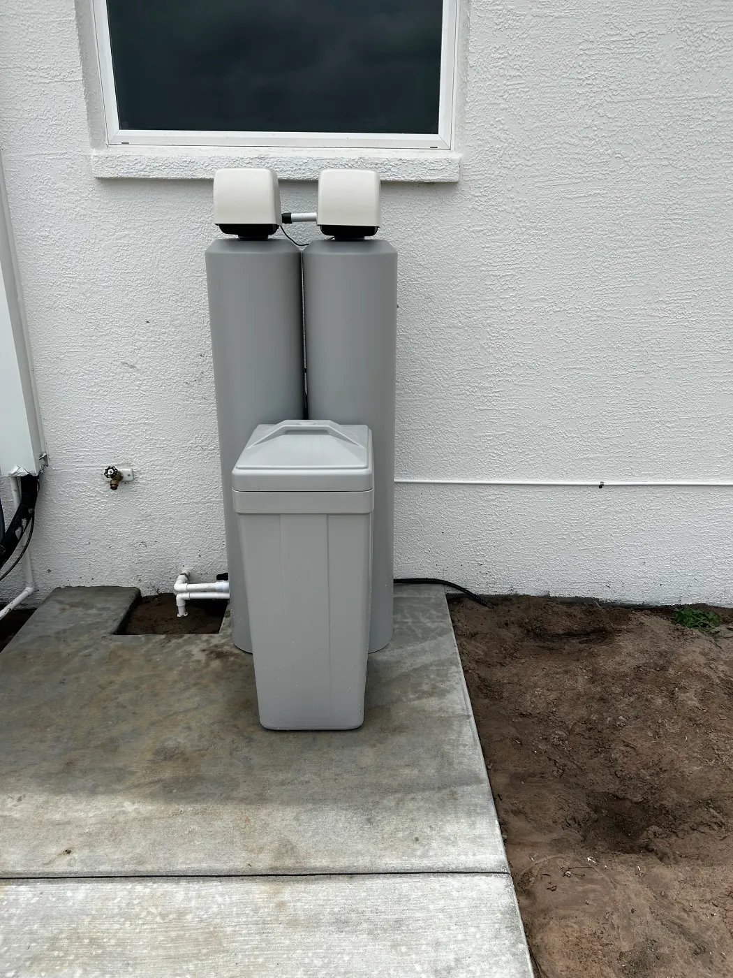 Twin-tank whole-home water treatment system and brine tank installed by Hydrology Water Solutions on an exterior concrete pad