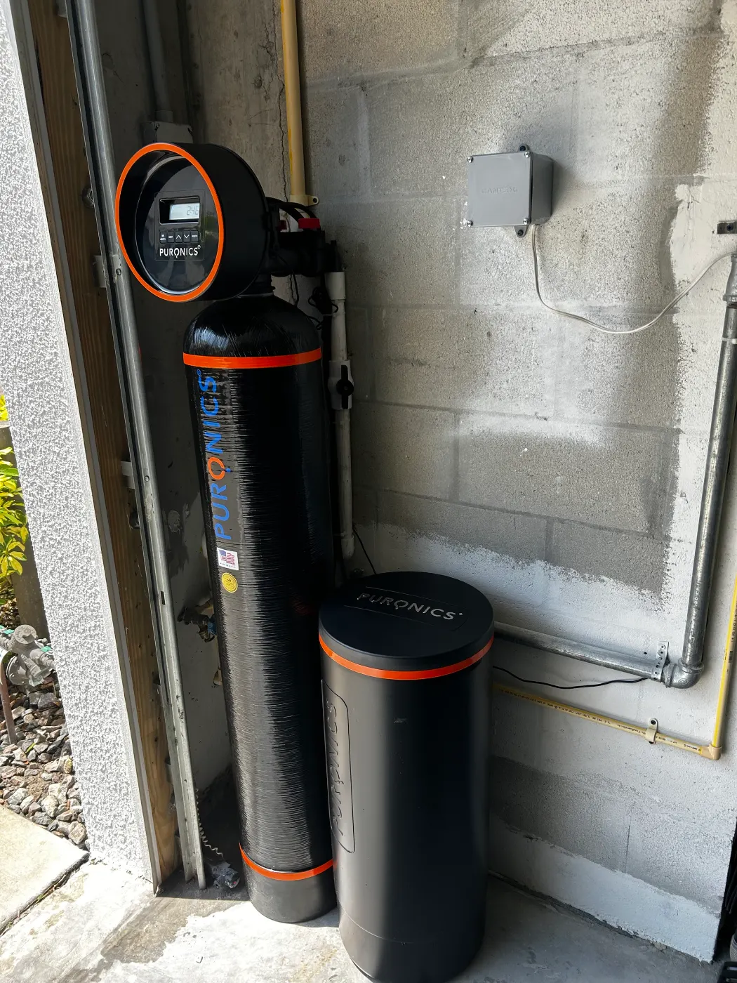 Puronics whole-home system and brine tank installed by Hydrology Water Solutions in a garage corner against a block wall