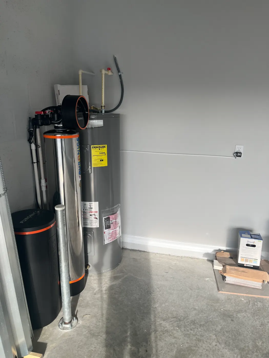 Puronics whole-home system installed by Hydrology Water Solutions beside a new electric water heater in a garage