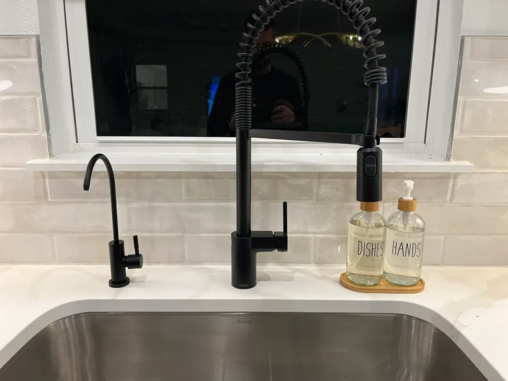 Matte black dedicated reverse osmosis drinking water faucet installed beside a matte black main kitchen faucet on a white quartz counter by Hydrology Water Solutions