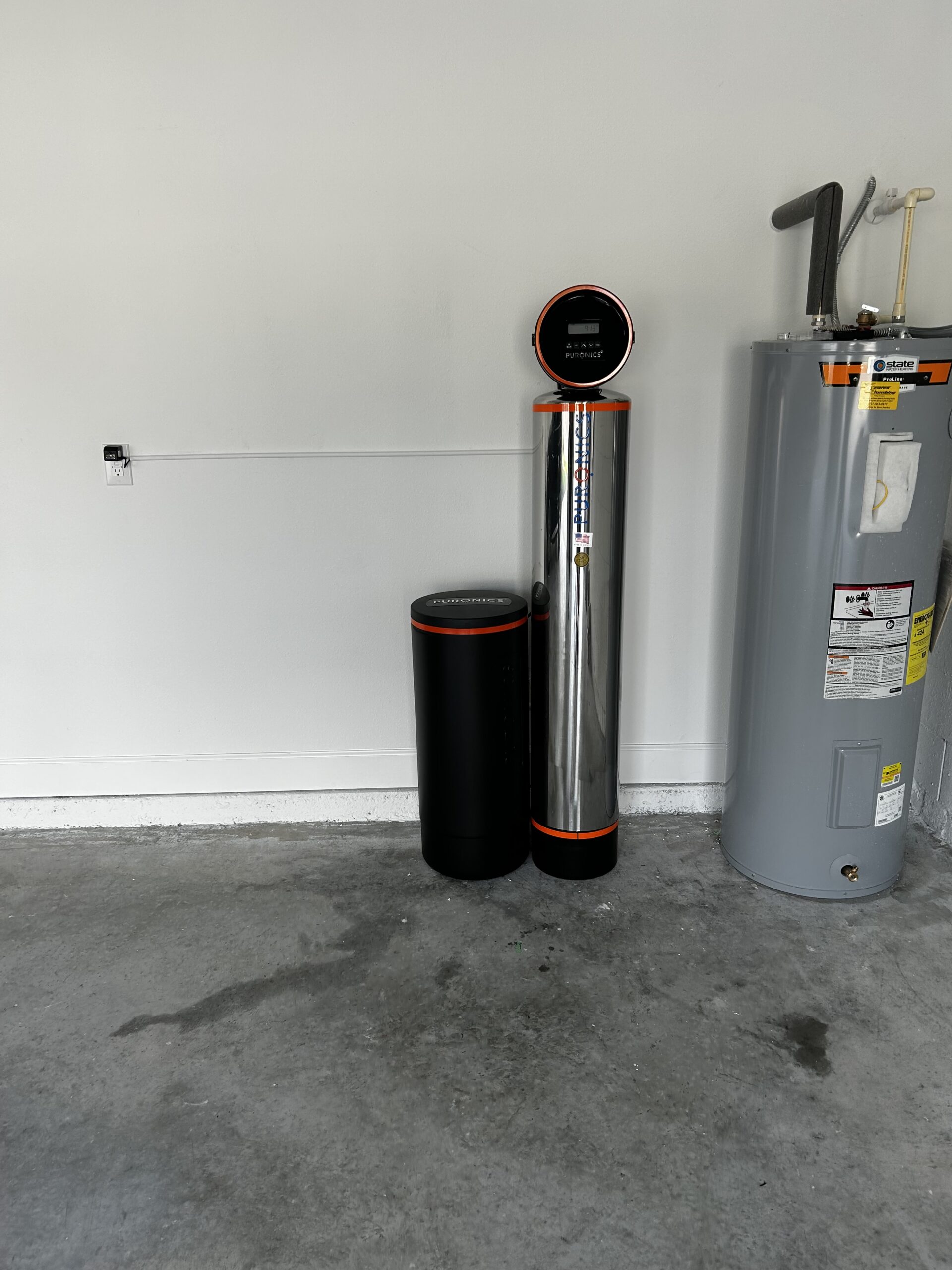 Puronics whole-home system installed in a garage beside the water heater by Hydrology Water Solutions